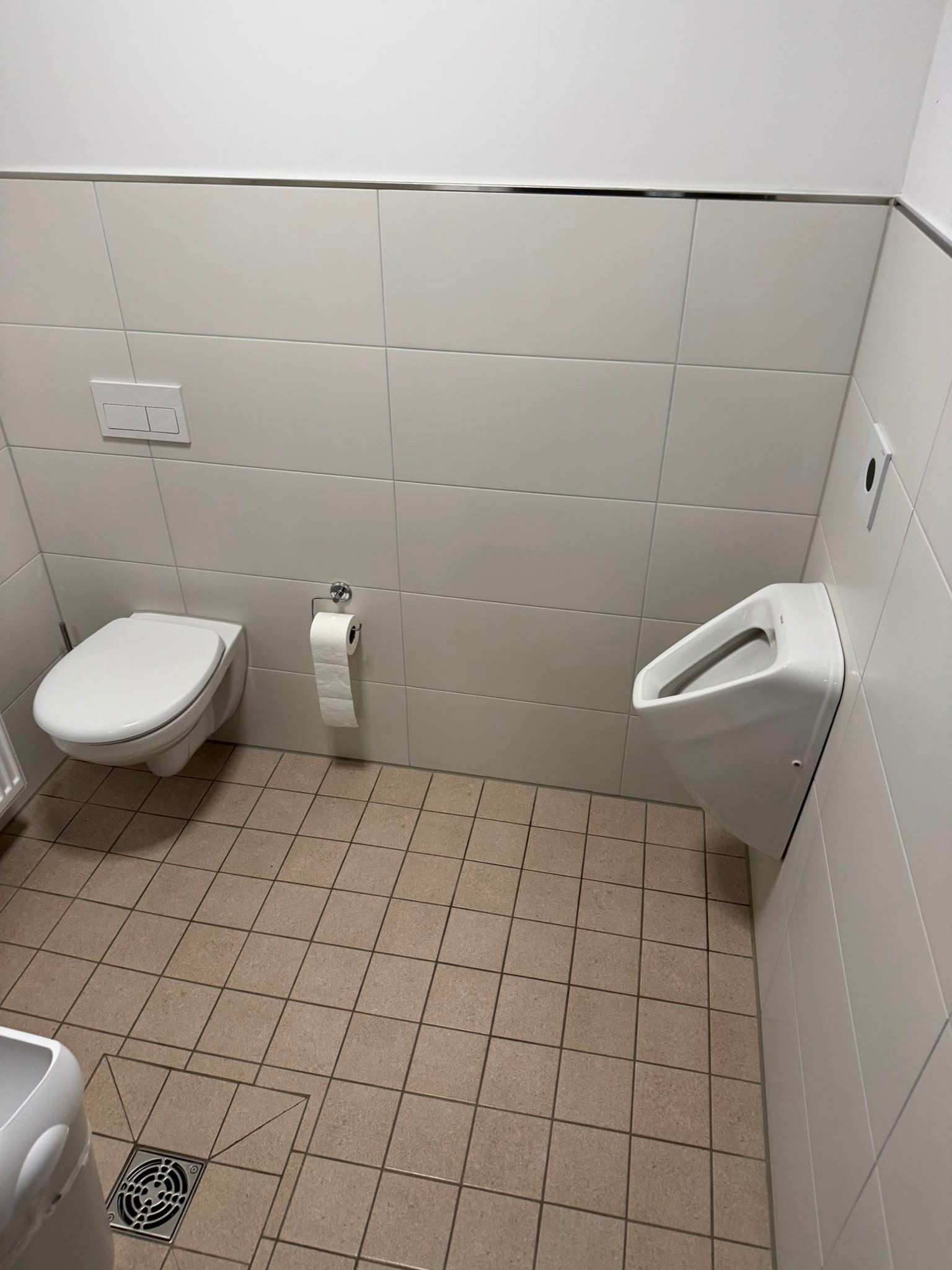 Sauberer Sanitärraum mit Toilette, Urinal und Bodenablauf