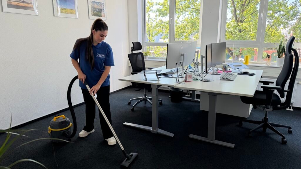 Jonas-Mitarbeiterin saugt Teppichboden zwischen Büroarbeitsplätzen.
