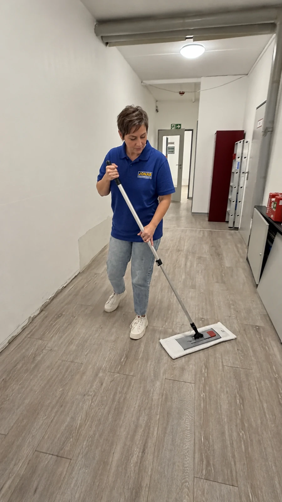 Reinigungskraft wischt einen Flurboden mit einem Flachmopp